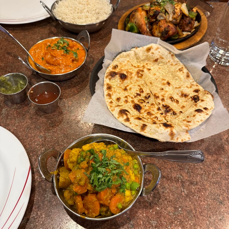 Indian feast with naan, rice, chicken tikka masala, vegetable curry, and sizzling tandoori chicken.