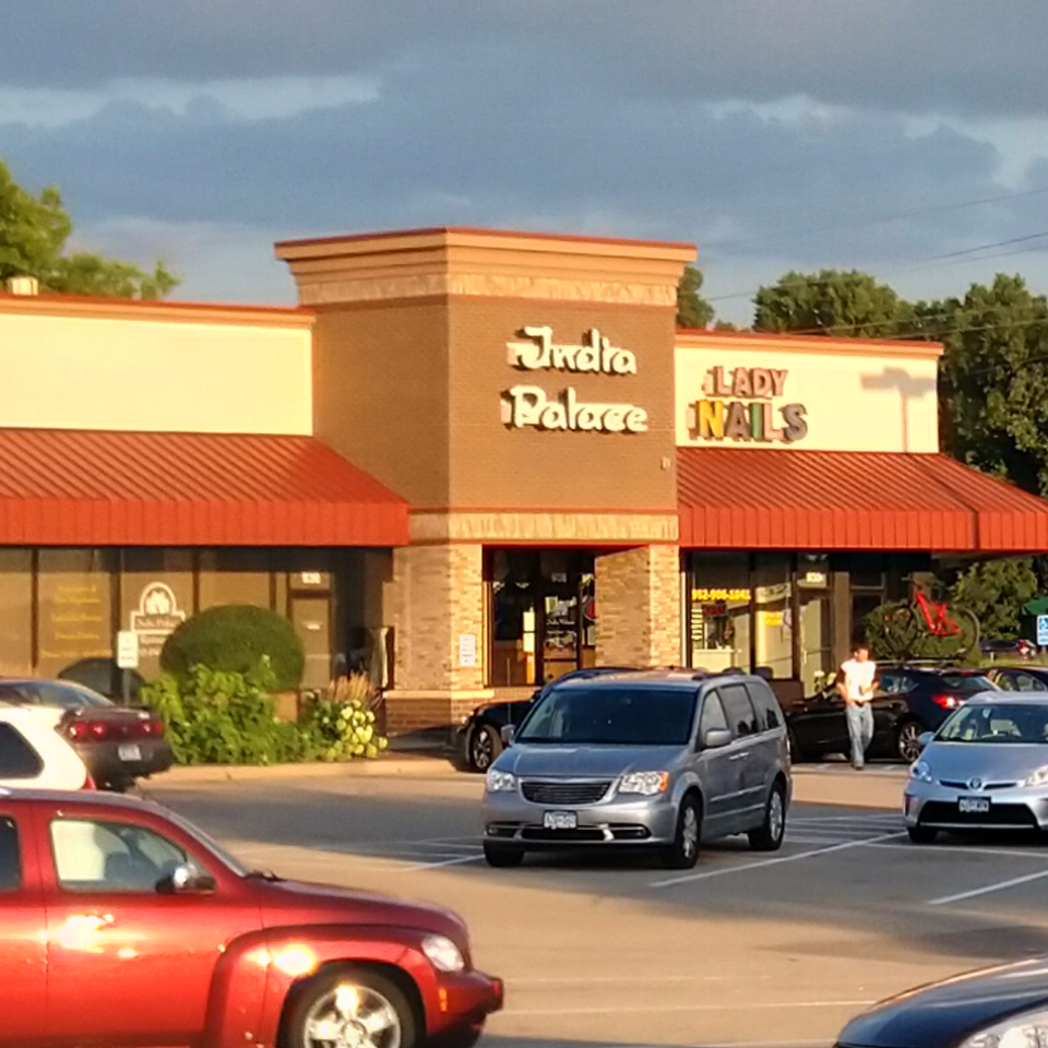 Exterior of India Palace restaurant with a parking lot full of cars under a cloudy sky.