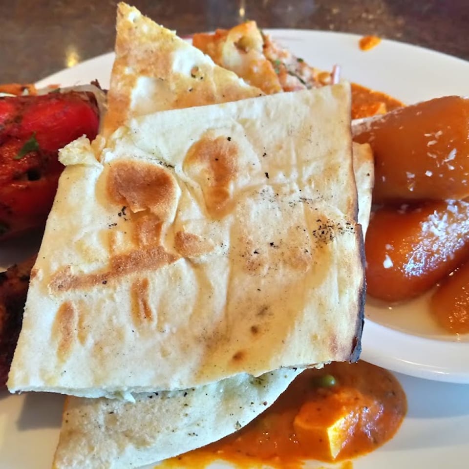 Naan bread, tandoori chicken, paneer curry, and gulab jamun on a white plate.