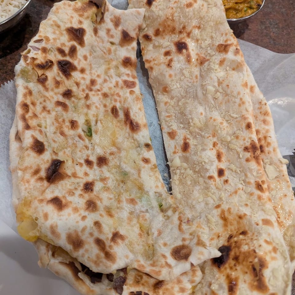 Garlic naan and stuffed naan served with rice and vegetable curry on a table.